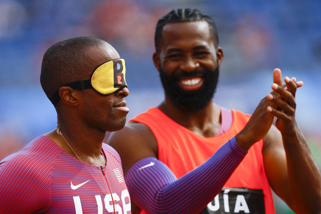 En la foto: para atleta y su guía. El para atleta con los ojos vendados y su guía aplaudiéndole mientras sonríe.